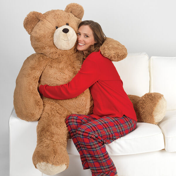 4' Big Hunka Love Bear - Seated golden brown bear with a female model in red pajamas on a sofa