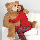 4' Big Hunka Love Bear - Seated golden brown bear with a female model in red pajamas on a sofa image number 7
