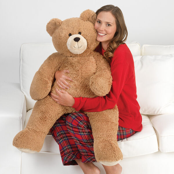 3' Hunka Love Bear - Seated golden brown bear with a model in red pajamas on a sofa