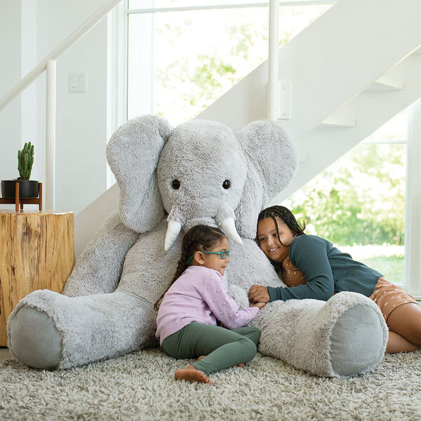 6' Giant Cuddle Elephant - Front view of seated grey plush elephant with girl models in a living room scene