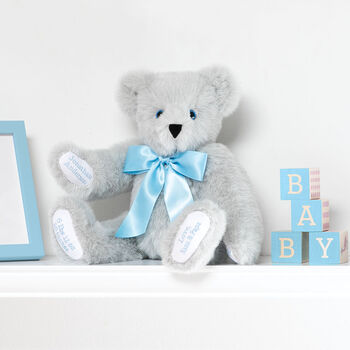 15" Premium Baby Boy Bear - Front view of seated jointed gray bear with white paw pads and chose of eye color wearing a blue satin bow in a bedroom scene. 