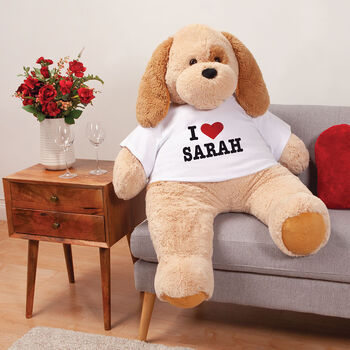 4' I HEART You T-Shirt Cuddle Puppy - Three quarter view of tan puppy wearing white t-shirt with "I Heart Sarah" graphic in black and red lettering in living room scene